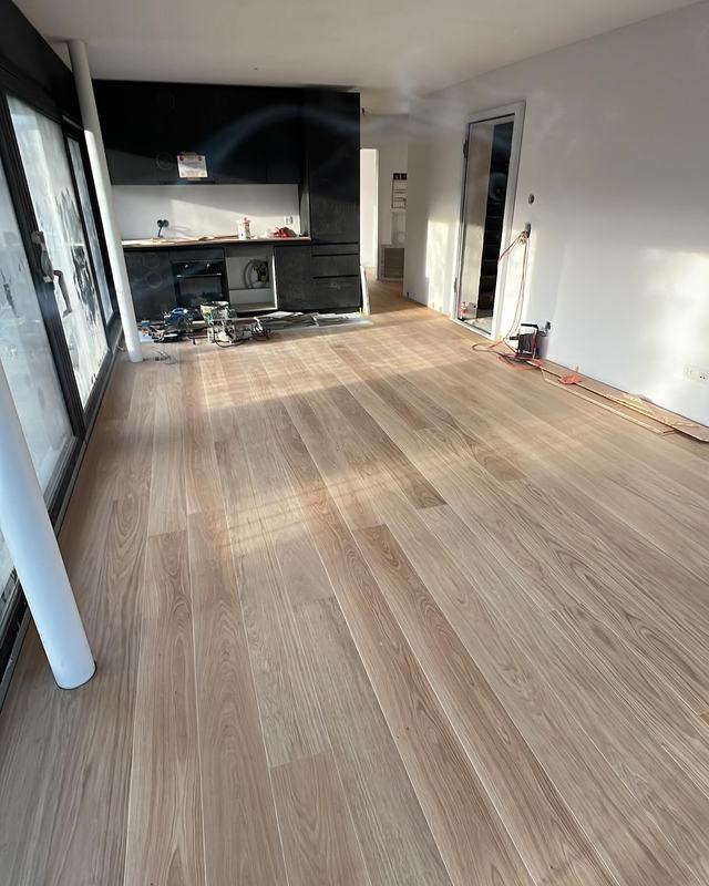 Grande pièce lumineuse avec parquet clair posé, baies vitrées